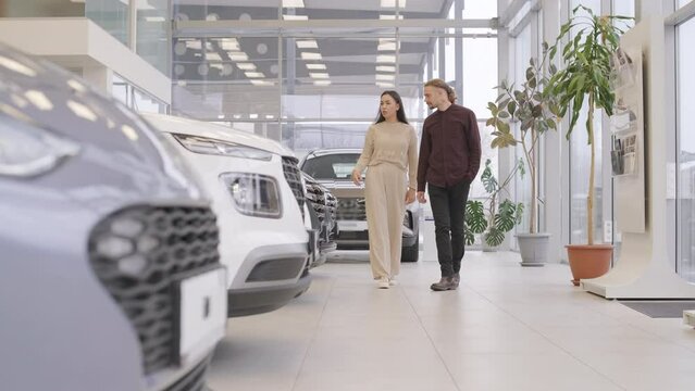 Beautiful young couple at car showroom choosing a new car to buy.