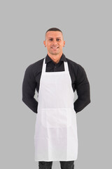 Attractive chef or waiter posing, wearing white apron and black shirt on gray background, in studio shot