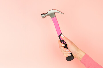 Renovation tools in the hands of a girl. Men's work is done by women's hands. Strong, but beautiful independent woman. Pink hammer in female hands on pink background. Woman's power