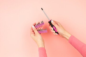 Renovation tools in the hands of a girl. Men's work is done by women's hands. Strong, but beautiful independent woman. Pink screwdriver and bits in female hands on pink background. Woman's power