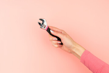 Renovation tools in the hands of a girl. Men's work is done by women's hands. Strong, but beautiful independent woman. Pink wrench in female hands on pink background. Woman's power