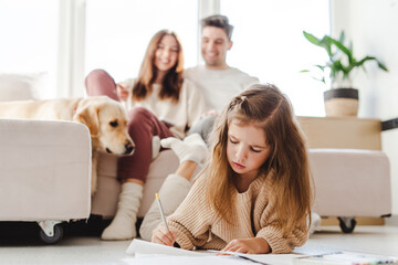 Happy attractive family, dog lying on sofa, little daughter sitting on floor drawing selective focus
