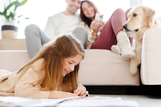 Smiling family, woman holding mobile phone, dog lying on sofa, little daughter sitting on floor