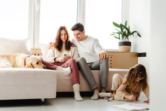 Positive family, man hugging woman, holding mobile phone, using smartphone, sitting on sofa in room