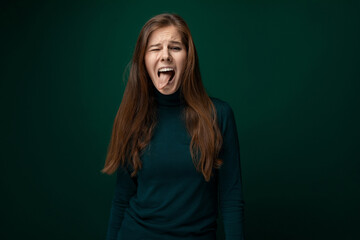 Portrait of a funny young woman with brown eyes dressed in a green turtleneck with a grimace