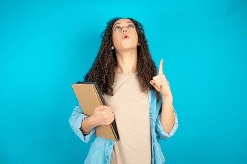 Fototapeta premium beautiful teen girl amazed and surprised looking up and pointing with fingers and raised arms.