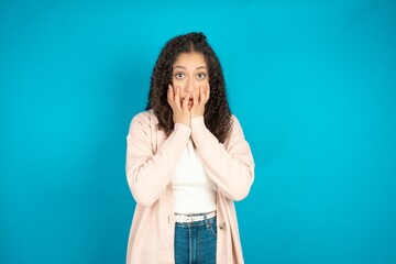 Stupefied beautiful teen girl expresses excitement and thrill, keeps jaw dropped, hands on cheeks,...