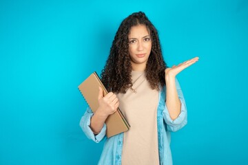 Fototapeta premium Indignant beautiful teen girl wearing denim jacket gestures in bewilderment, frowns face with dissatisfaction.
