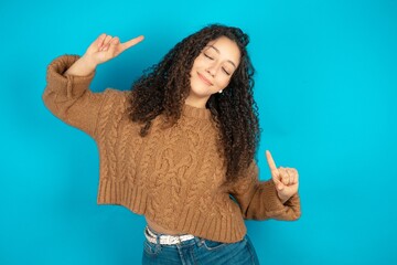 Photo of upbeat beautiful teen girl wearing brown knitted sweater  has fun and dances carefree wear...