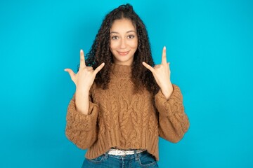 beautiful teen girl wearing brown knitted sweater makes rock n roll sign looks self confident and...