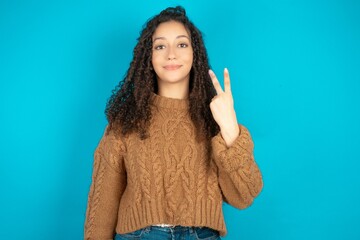 beautiful teen girl wearing brown knitted sweater smiling and looking friendly, showing number two...