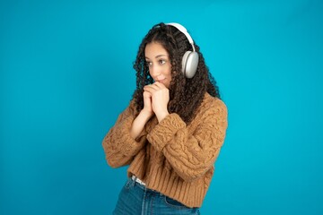 beautiful teen girl wearing brown knitted sweater wears stereo headphones listening to music concentrated and looking aside with interest.