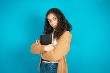 Portrait of beautiful teen woman wearing beige knitted jacket standing with folded arms and smiling