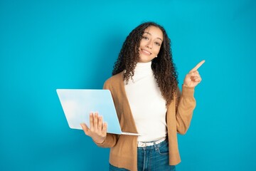 beautiful teen woman wearing beige knitted jacket directing empty space  hold laptop