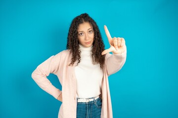 Beautibul teen girl wearing casual clothes making fun of people with fingers on forehead doing loser gesture mocking and insulting.