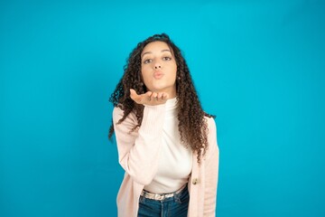 Beautibul teen girl wearing casual clothes looking at the camera blowing a kiss with hand on air being lovely and sexy. Love expression.