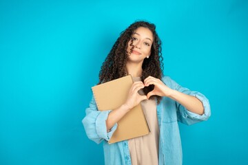 beautiful arab student carries notebooks smiling in love doing heart symbol shape with hands. Romantic concept.
