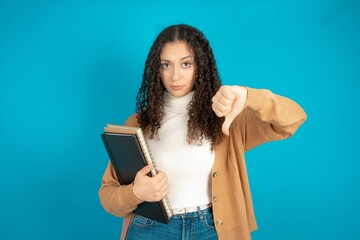 beautiful arab student carries notebooks looking unhappy and angry showing rejection and negative with thumbs down gesture. Bad expression.