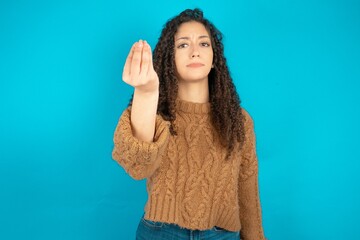 Beautiful teen girl wearing knitted sweater over blue background Doing Italian gesture with hand...