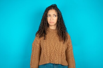 Dissatisfied Beautiful teen girl wearing knitted sweater over blue background purses lips and has...