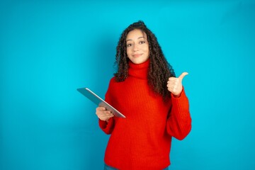 beautiful teen girl wearing red knitted sweater pointing empty space modern device