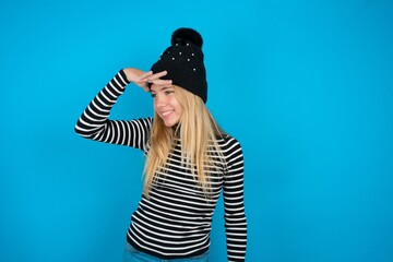 Teen caucasian girl wearing striped sweater and woolly hat very happy and smiling looking far away...