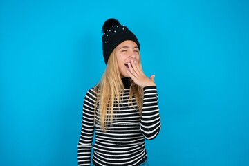 Teen caucasian girl wearing striped sweater and woolly hat being tired and yawning after spending...
