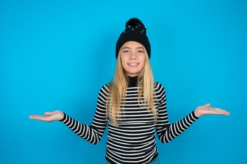 Cheerful cheery optimistic Teen caucasian girl wearing striped sweater and woolly hat holding two...