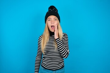 Shocked Teen caucasian girl wearing striped sweater and woolly hat looks with great surprisment...