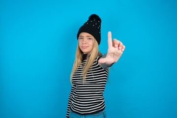 Teen caucasian girl wearing striped sweater and woolly hat making fun of people with fingers on...