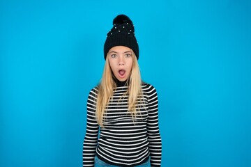 Oh my God. Surprised Teen caucasian girl wearing striped sweater and woolly hat stares at camera...