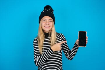Smiling Teen caucasian girl wearing striped sweater and woolly hat Mock up copy space. Pointing...