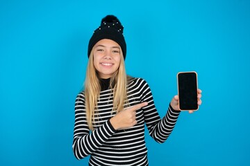 Attractive cheerful Teen caucasian girl wearing striped sweater and woolly hat holding in hands...