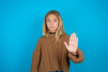 beautiful caucasian teen girl wearing yellow sweater shows stop sign prohibition symbol keeps palm...