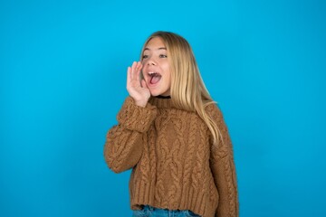 beautiful caucasian teen girl wearing brown sweater look empty space holding hand face and screaming or calling someone.