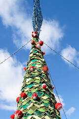 Christmas tree decorated with red and green balls against the blue sky. Handmade crochet Christmas tree.
