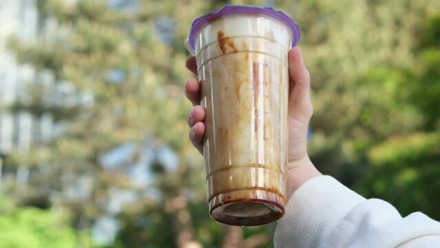 Bubble Milk Tea plastic glass of fresh milk with Kuromitsu black sugar syrup and Boba hot black pearl on a skyscraper city background in a girl hand, Taiwanese drinking culture