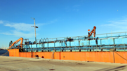 Large orange empty barge cargo ship standing at the pier against the blue sky