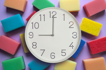 9 o'clock, morning. Cleaning time. White wall clock on background of multi-colored kitchen sponges....