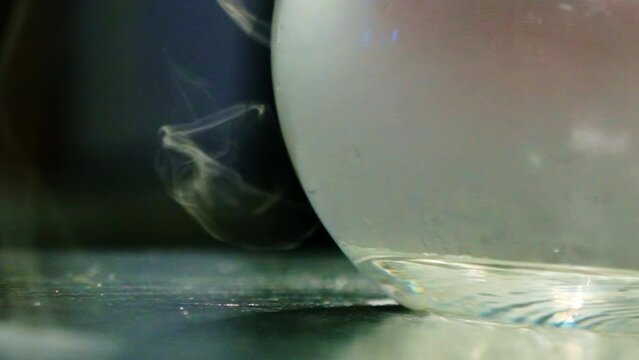 Transparent bowl encircled by sinuous wisps of bending smoke positioned on kitchen table. Light steam veil enveloping glass nitro bowl