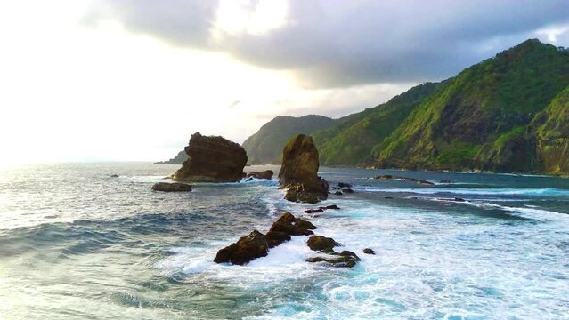 Drone shot on Papuma Beach, Jember, Indonesia with thick vegetations, towering cliff and ocean waves.