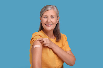 Senior woman with adhesive bandage on her arm after vaccination against light blue background - obrazy, fototapety, plakaty