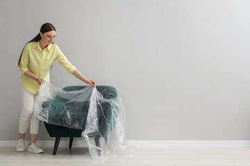 Young woman putting plastic film away from armchair near light grey wall indoors. Space for text