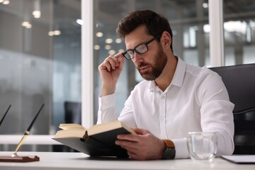 Handsome man reading book at table in office. Lawyer, businessman, accountant or manager