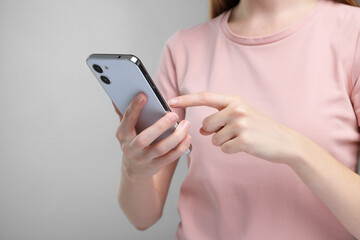 Woman sending message via smartphone on grey background, closeup