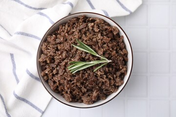 Fried ground meat in bowl and rosemary on white tiled table, top view