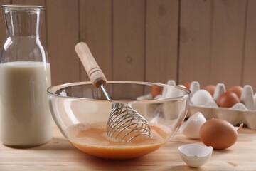 Making dough. Beaten eggs in bowl, shells and milk on wooden table, closeup