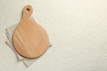 Wooden cutting board and napkin on white textured table, top view. Space for text