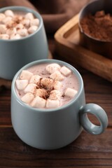 Cups of aromatic hot chocolate with marshmallows and cocoa powder on table, closeup