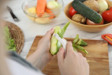 Woman peeling fresh zucchini at white marble table, closeup